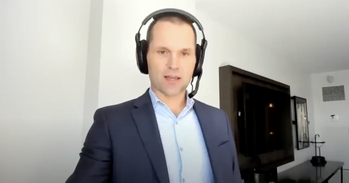 man wearing suit and headset talks to camera